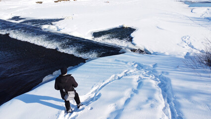 Man overlooking a partially frozen winter river under a bright blue sky