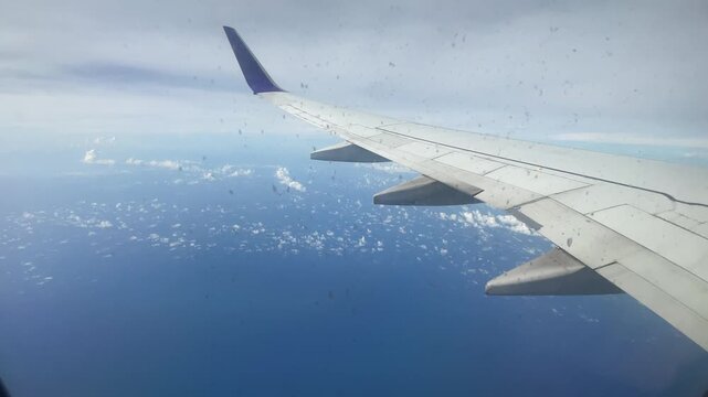 Airplane Wing Flying Above Blue Ocean Water and White Fluffy Clouds