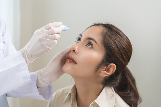 Health care concept, eye doctor eye drops to asian young woman patient, hand using medical eye drop to treat dry eye, suffering irritation or inflammation, allergy optical symptom at optic clinic.