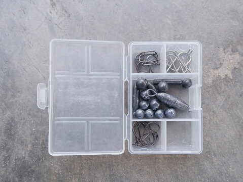 a transparent tackle box with fishing hooks and lead sinkers on a grey background. Essential fishing equipment for anglers