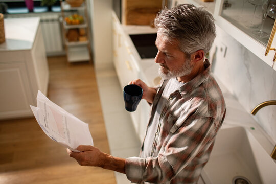 Mature man reading bills with coffee in home kitchen