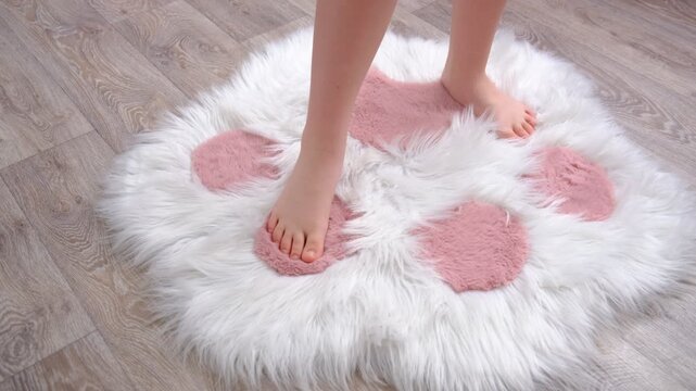 Barefoot teenager girl  touching fluffy carpet and enjoying its softness and warmth. The plush carpet felt silky smooth, making every step a joy. Simplicity of life and the warmth of being at home.