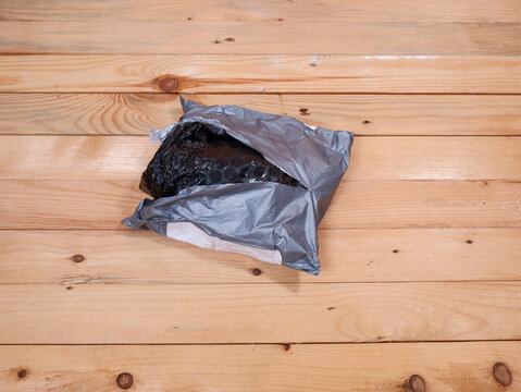 Opened gray plastic shipping bag revealing black bubble wrap on a wooden table. Unboxing e-commerce parcel, delivery package received