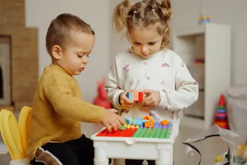 Fototapete Lego Two young children play together on a small table, building structures with colorful blocks in a bright playroom during the afternoon  © sementsova321