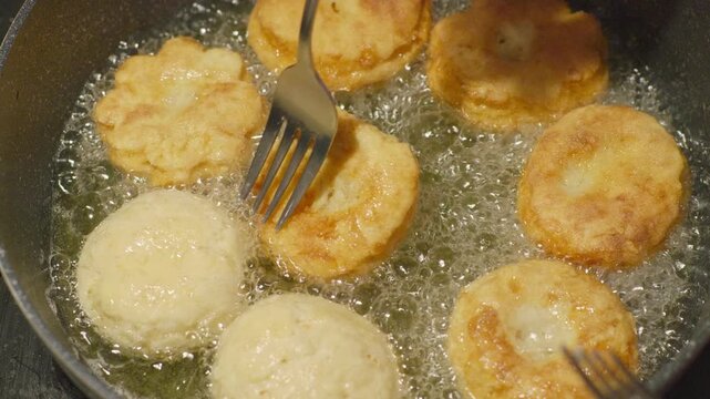 Hands using fork to flip European made healthy style doughnuts frying in a pan