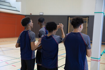 African American teen males in navy shirts standing back-to-camera near padded pole in school gym