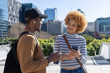 Diverse friends chatting on terrace, man with backpack holding mug, woman holding smartphone