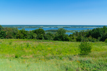 Fototapeta premium Beautiful high angle view of a vast river valley with lush green forests and wild meadows on a sunny summer day under a clear blue sky