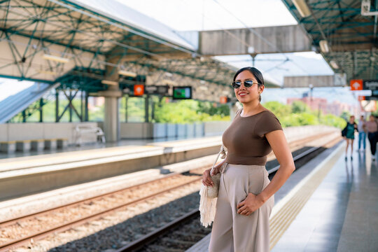 Confident and smiling young Latina woman waiting for a train at a clean and bright Metro station in Medellin, Colombia. Wears modern casual clothing sunglasses, enjoying a warm, sunny day in the city