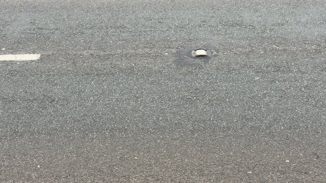 Static high angle shot of a wet asphalt road surface with a catseye reflective stud and white lane markings