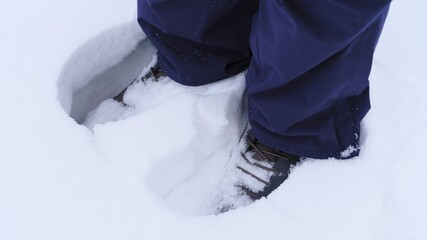 Close-up of a person wearing dark blue snow pants and boots standing in deep white snow.