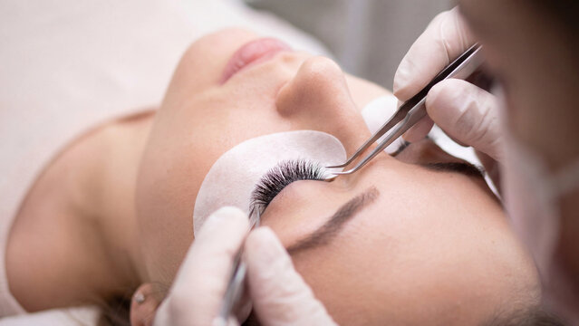 Professional esthetician applying eyelash extensions during precision beauty treatment procedure at salon
