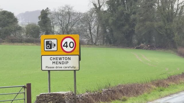 Roadside view of a yellow speed camera warning sign and forty mile speed limit for Chewton Mendip village
