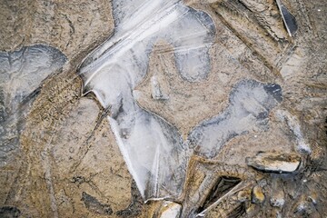 Abstraktes Motiv mit wei&szlig;em Eismuster &uuml;ber braunem gefrorenem Erdboden in der Natur bei K&auml;lte, Frost und Eis im Winter