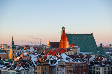 Obraz premium Warsaw Old Town panorama showcasing rooftops covered in snow during a winter sunset, highlighting historic buildings and Cathedral of St. John the Baptist