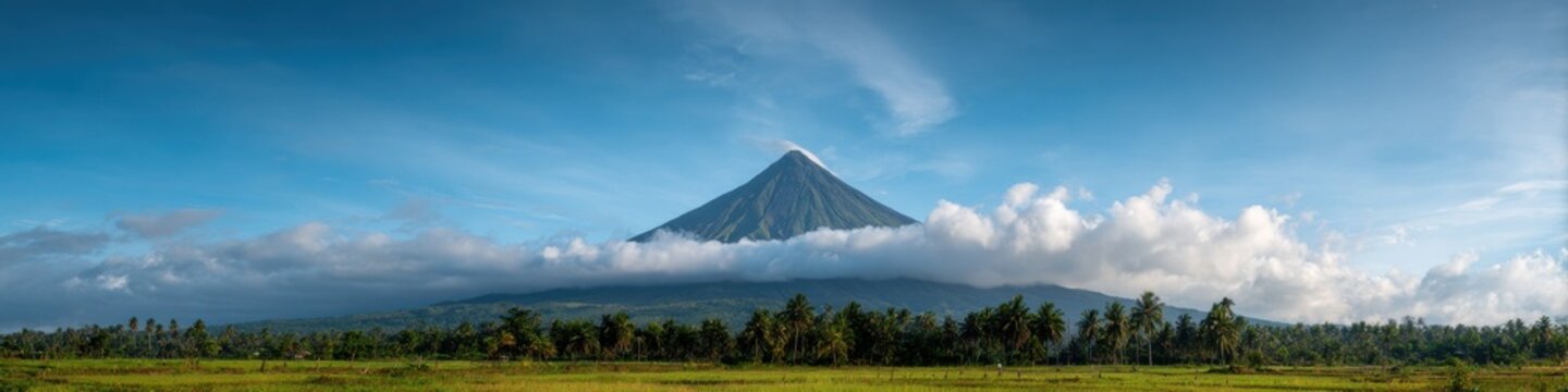 Majestic mayon volcano with lush greenery and clouds in clear blue sky