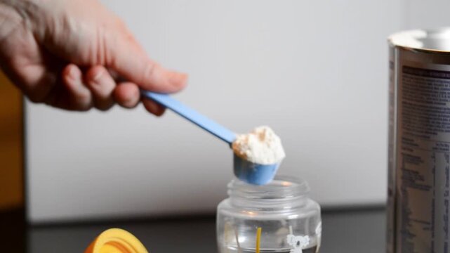 Preparing baby formula by putting a scoop of milk powder in the bottle with water