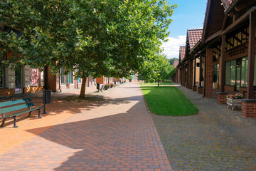 Obraz premium Beautiful sunny day on a modern pedestrian street with green lawns, leafy trees, and brick architecture in a European style shopping mall area