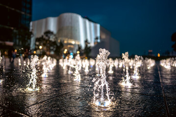 slow motion of illuminated stylish fountain jets in modern city at night, glowing water streams at urban plaza at dusk