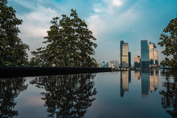 city skyline with skyscrapers reflected in calm water of lake or swimming pool at sunset, Modern cityscape of Bangkok with highrise towers mirrored on tranquil waterfront under evening sky