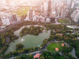 Aerial drone view of Lumpini Park lake surrounded by Bangkok skyline and urban greenery, Panorama of cityscape and urban parkland in Thailand with skyscrapers and nature contrast