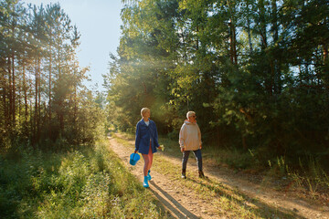 Obraz premium Two women walk along a dirt path surrounded by tall trees during a clear sunny day in a forested area