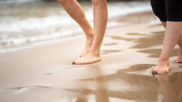Barefoot feet walking on wet beach sand near shoreline close-up