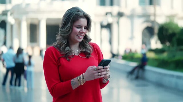 Young Latina woman smiling brightly while taking a selfie, sitting relaxed on a ledge outside Palacio de Bellas Artes in Mexico City during a sunny morning, wearing casual red top and blue jeans