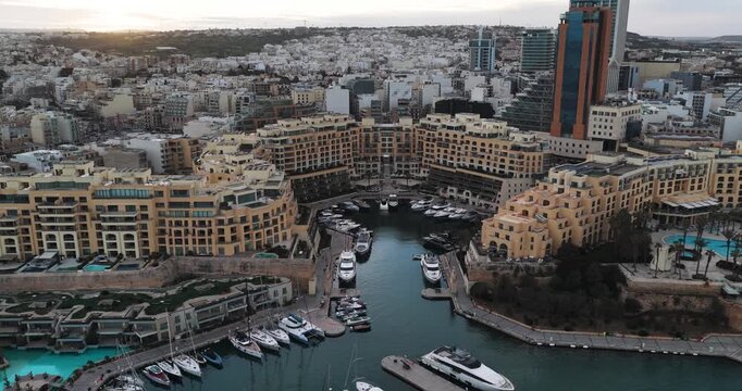 Aerial view of Portomaso Marina's turquoise waters filled with yachts, surrounded by the golden hues of buildings, St. Julian, Malta.