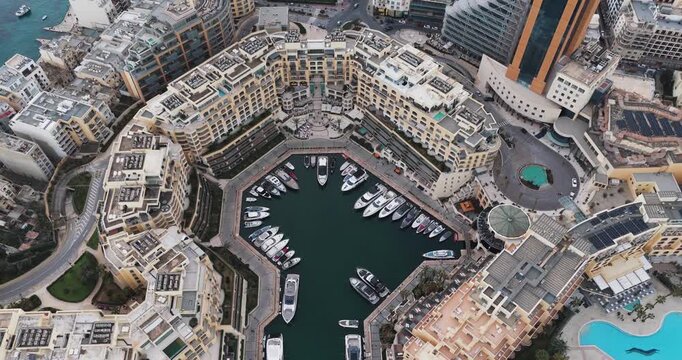 Aerial view of Portomaso Marina's luxury yachts nestled in the turquoise waters, surrounded by golden buildings and pools, St. Julian, Malta.