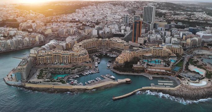 Aerial view of the Portomaso marina, lined with yachts, and surrounded by luxury buildings with the city skyline as a backdrop, St. Julian, Malta.