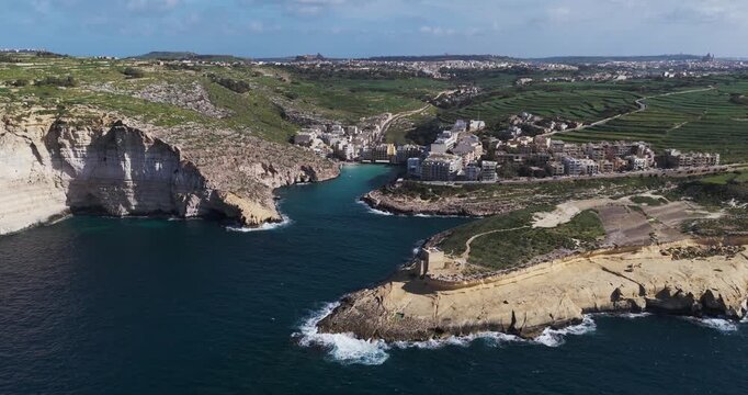 Aerial view of the stunning Xlendi Bay where the buildings meet the sea surrounded by rugged cliffs and green hills, Xlendi, Munxar, Malta.