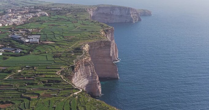 Aerial view of rugged cliffs meeting the vast expanse of the blue sea, showcasing the contrast between nature's textures and tones, Xlendi, Munxar, Malta.