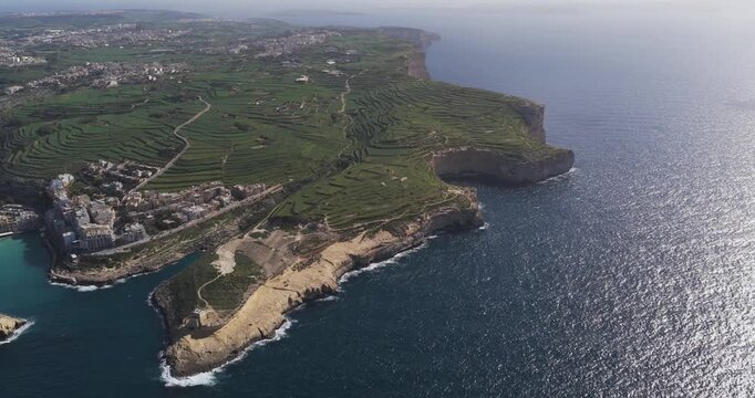 Aerial view of Xlendi Bay reveals the turquoise waters contrasting against the rugged coastline and lush green terraces, Xlendi, Munxar, Malta.