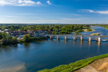 Fototapeta premium Wide aerial perspective of La Charite sur Loire in central France, featuring a historic stone bridge crossing the Loire river, traditional rooftops, and lush greenery along the riverside. The scene