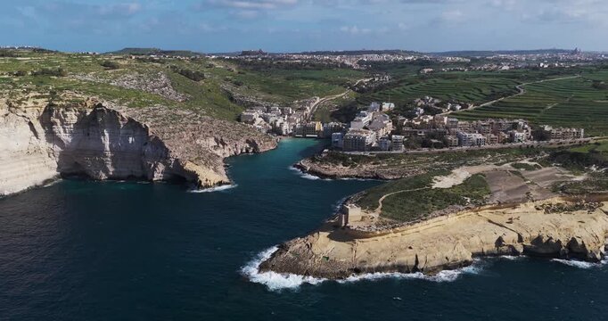 Aerial view of Xlendi Bay's white buildings nestled between rugged cliffs and the deep blue sea, creating a striking contrast, Xlendi, Munxar, Malta.