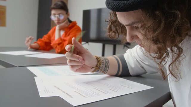 Side view close up shot of tattooed young woman as female inmate writing on paper while doing tasks during class in prison education program, copy space