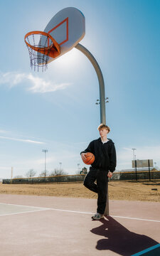 Young Man Leans Against an Outdoor Basketball Hoop