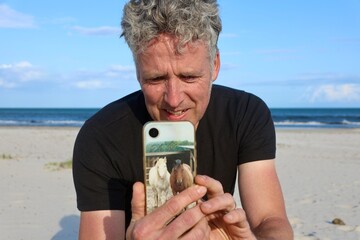 Man Using Smartphone at the Beach While Taking a Photo
