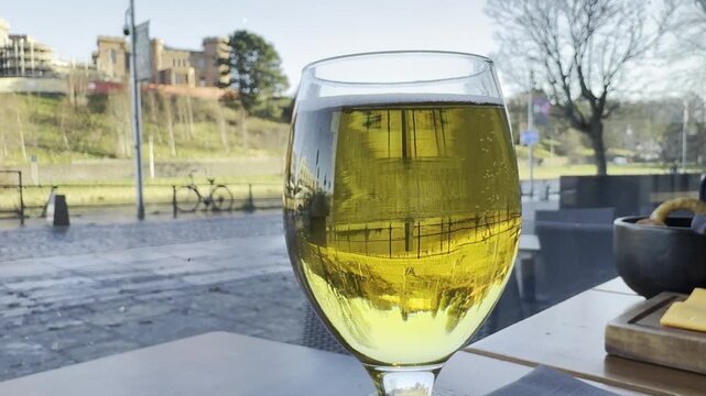 A table by the window in a city cafe. A close-up of a glass of beer with bubbles inside. The embankment and road are in the background.