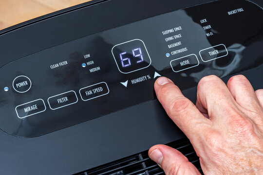 Close-up of hand adjusting humidity settings on a home dehumidifier control panel display.
