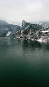 Vertical 4K shot of medieval Strecno Castle on a snowy cliff above the Vah river in winter. Historic Slovakian fortress with an old river ferry and Mala Fatra mountains. Slovakia mobile video.