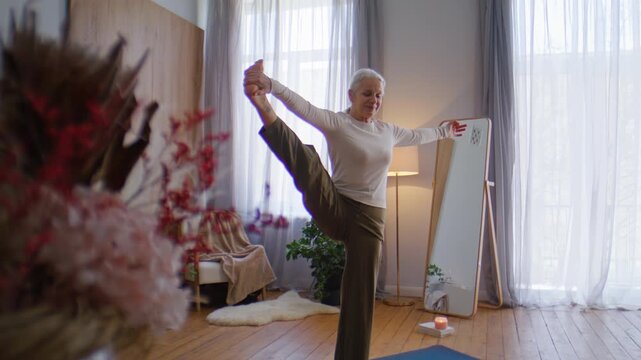 Elderly woman holds high leg extension staying proud and calm