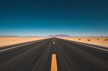 asphalt road stretching through desert landscape with mountain in distance under clear blue sky
