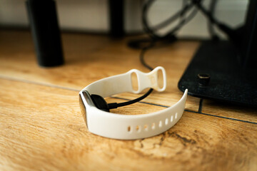 Charging fitness bracelet lying on the floor, connected to power source. Modern technology device replenishing battery. Perfect for concepts of health tracking, smart gadgets, daily lifestyle.