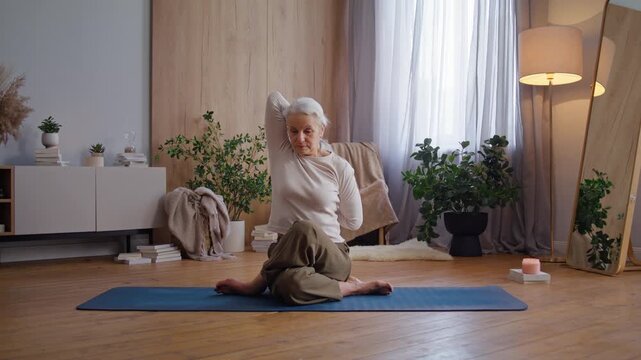 Senior woman performs seated spinal twist at yoga stretch on mat