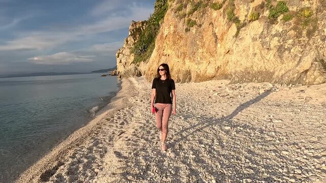 A tourist walks along the coast at sunset on a rocky beach.
