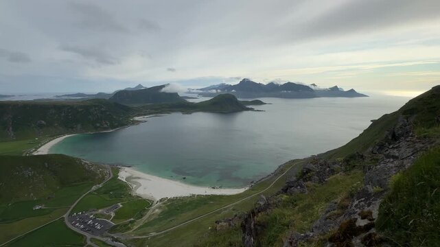 Cinematic panoramic footage of the stunning Haukland Beach coastline with turquoise sea, white sand, and dramatic mountain peaks in Lofoten, Norway