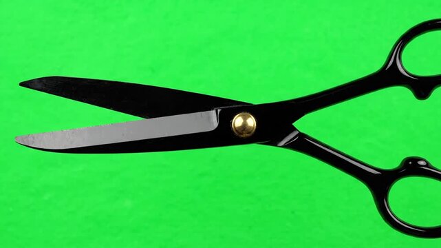 Close-up of black scissors opening and closing on a vibrant green screen background.