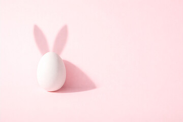 Fototapeta premium Minimal Easter egg with bunny ears on soft pink background, modern holiday concept